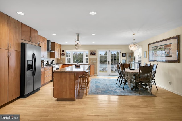 kitchen with appliances with stainless steel finishes, pendant lighting, a kitchen breakfast bar, a center island, and wall chimney exhaust hood