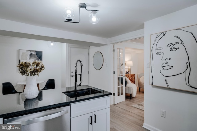 kitchen with light wood-type flooring, stainless steel dishwasher, sink, and white cabinets