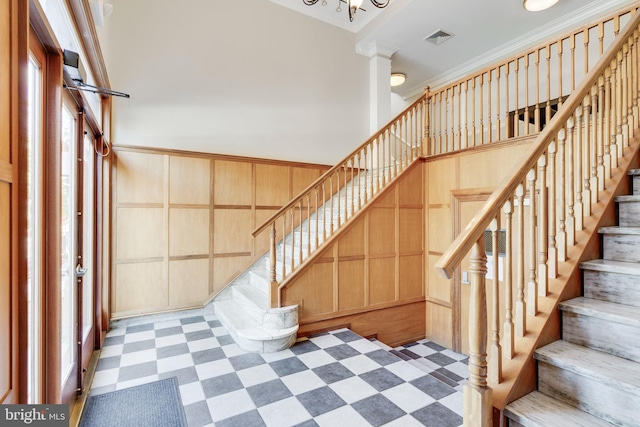 stairway with decorative columns, ornamental molding, and wood walls