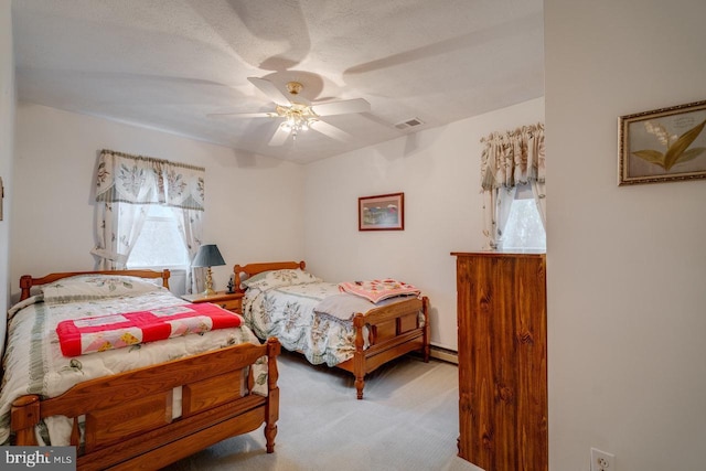 bedroom with ceiling fan, light colored carpet, baseboard heating, and a textured ceiling