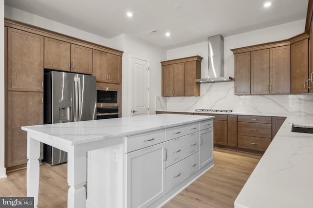 kitchen featuring stainless steel appliances, light stone countertops, a center island, and wall chimney exhaust hood