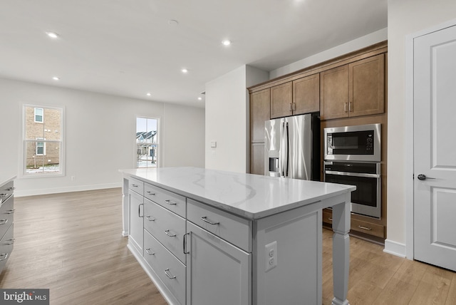 kitchen featuring a kitchen island, light stone countertops, appliances with stainless steel finishes, and light hardwood / wood-style floors