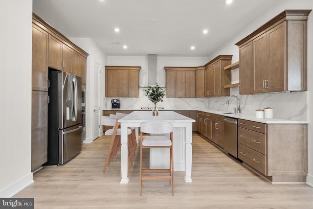 kitchen with a kitchen island, backsplash, stainless steel appliances, wall chimney range hood, and light wood-type flooring