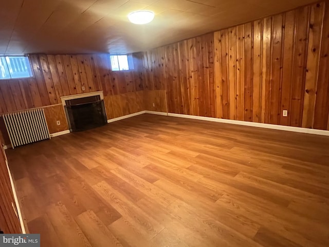 basement featuring wooden walls, radiator, and hardwood / wood-style floors