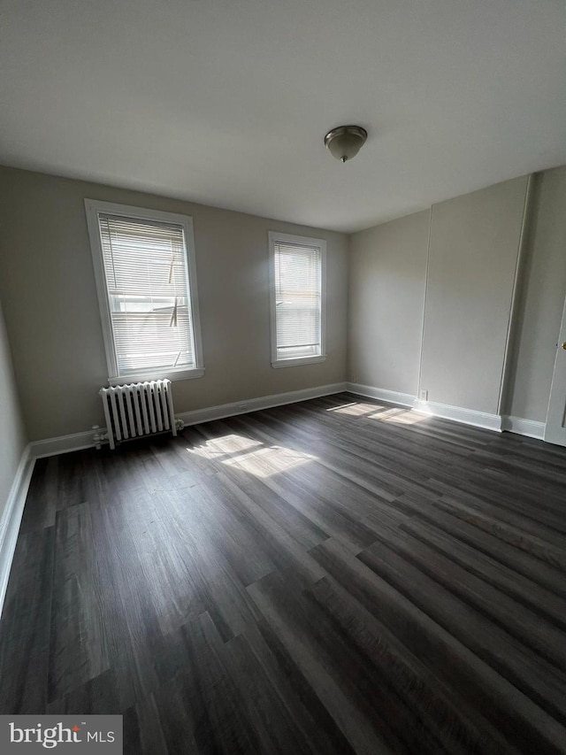 empty room with dark wood-type flooring and radiator heating unit