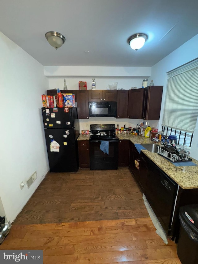 kitchen featuring sink, hardwood / wood-style floors, dark brown cabinetry, black appliances, and light stone countertops