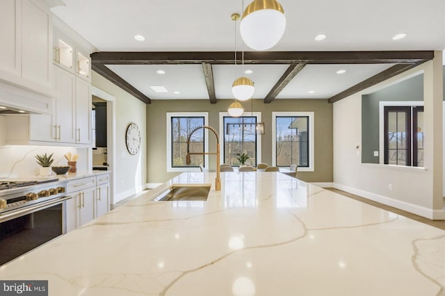 kitchen with decorative light fixtures, white cabinetry, sink, light stone counters, and gas range