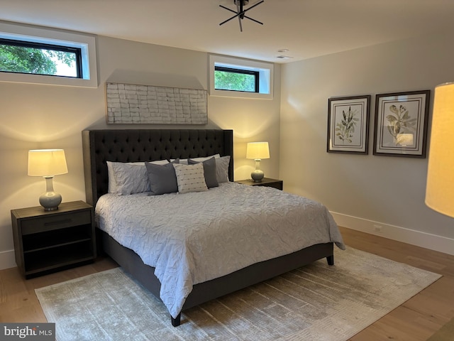 bedroom with multiple windows, wood finished floors, and baseboards