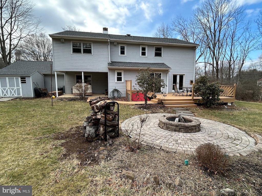 rear view of house featuring a wooden deck, a fire pit, a storage shed, and a yard