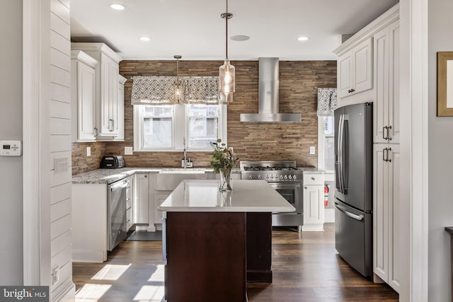 kitchen with a kitchen island, stainless steel appliances, light countertops, wall chimney range hood, and white cabinetry