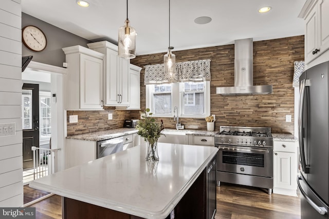 kitchen with wall chimney exhaust hood, appliances with stainless steel finishes, decorative light fixtures, a center island, and white cabinetry