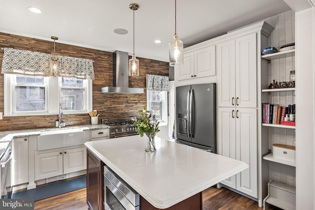 kitchen with wall chimney exhaust hood, appliances with stainless steel finishes, light countertops, white cabinetry, and a sink