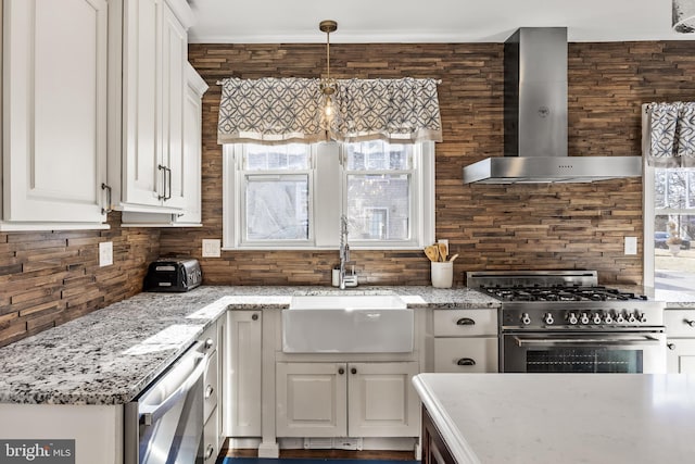 kitchen featuring wall chimney exhaust hood, stainless steel appliances, white cabinetry, pendant lighting, and a sink