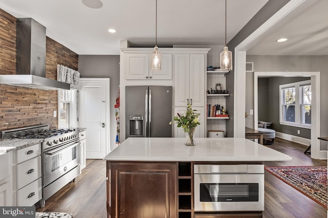 kitchen featuring wall chimney exhaust hood, hanging light fixtures, white cabinets, and stainless steel appliances