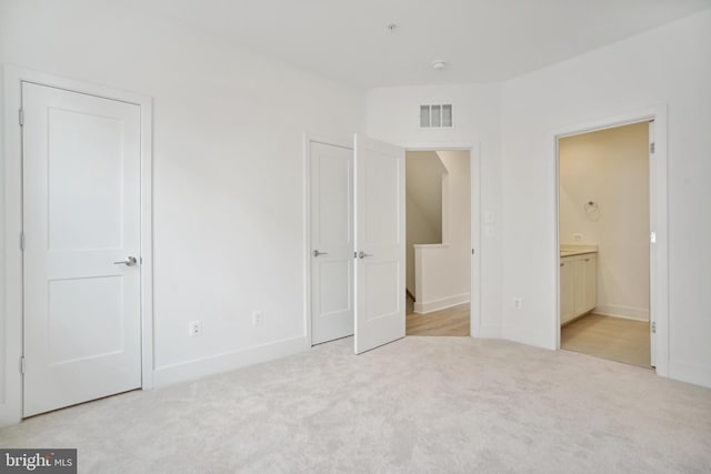 unfurnished bedroom with ensuite bath and light carpet