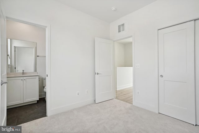 unfurnished bedroom featuring ensuite bath, sink, and light colored carpet