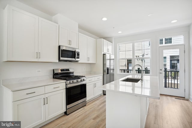 kitchen with white cabinets, appliances with stainless steel finishes, sink, and a kitchen island with sink