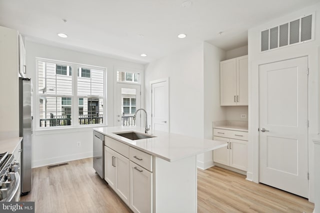 kitchen with white cabinetry, a center island with sink, light hardwood / wood-style floors, sink, and appliances with stainless steel finishes