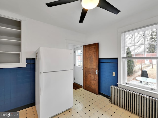 kitchen with ceiling fan, radiator, white fridge, and tile walls