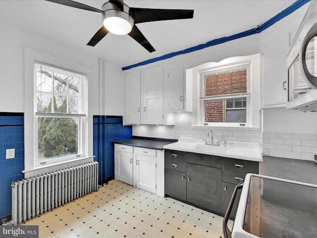 kitchen featuring white cabinetry, radiator, sink, and tile walls