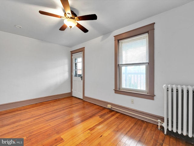 unfurnished room featuring a wealth of natural light, radiator, hardwood / wood-style floors, and ceiling fan