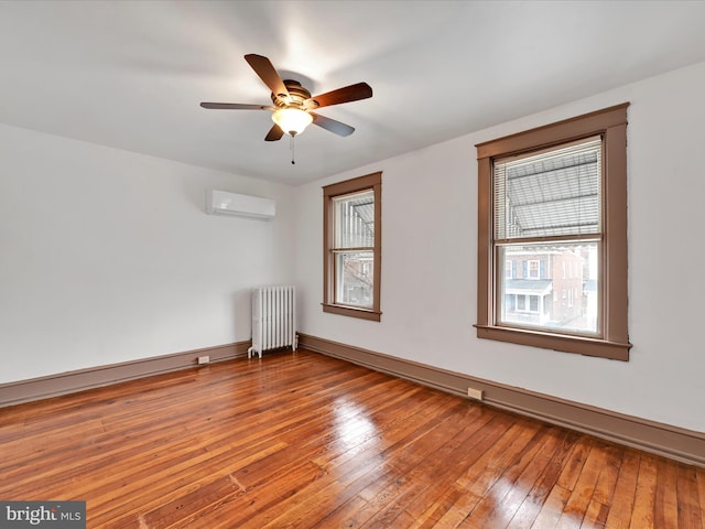 empty room featuring hardwood / wood-style flooring, ceiling fan, radiator heating unit, and a wall unit AC