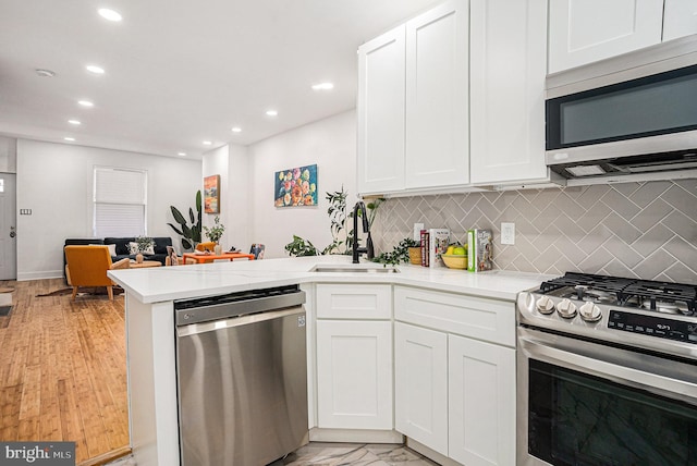 kitchen with appliances with stainless steel finishes, a peninsula, light stone countertops, white cabinetry, and a sink