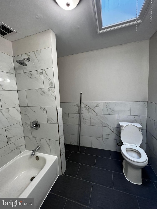 bathroom featuring tile walls, toilet, and tiled shower / bath