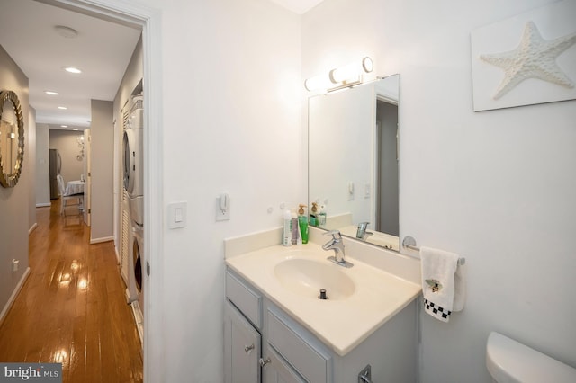 bathroom featuring stacked washer and dryer, wood-type flooring, vanity, and toilet