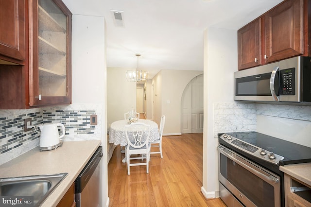 kitchen with pendant lighting, stainless steel appliances, tasteful backsplash, light hardwood / wood-style floors, and a chandelier