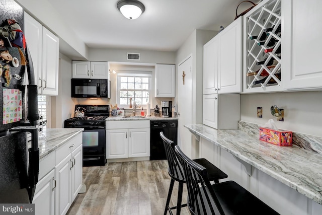 kitchen with sink, light stone counters, black appliances, light hardwood / wood-style flooring, and white cabinets