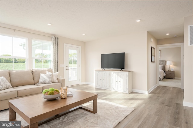 living room with a textured ceiling, light wood-type flooring, and baseboards