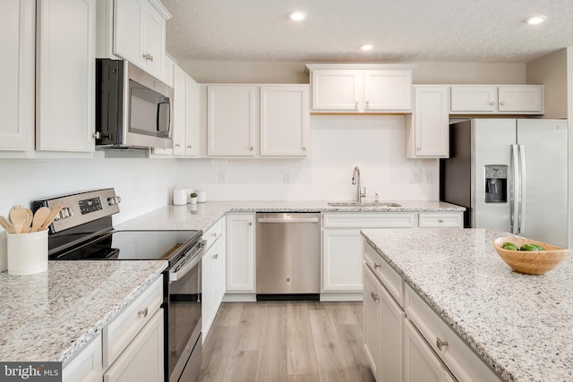 kitchen featuring sink, white cabinets, light stone counters, stainless steel appliances, and light hardwood / wood-style flooring