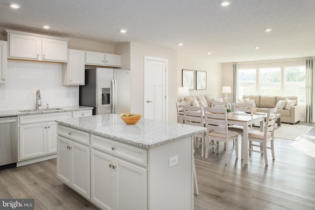 kitchen featuring a sink, a kitchen island, tasteful backsplash, stainless steel appliances, and light wood finished floors