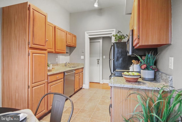 kitchen featuring dishwasher, sink, light stone countertops, and light tile patterned floors