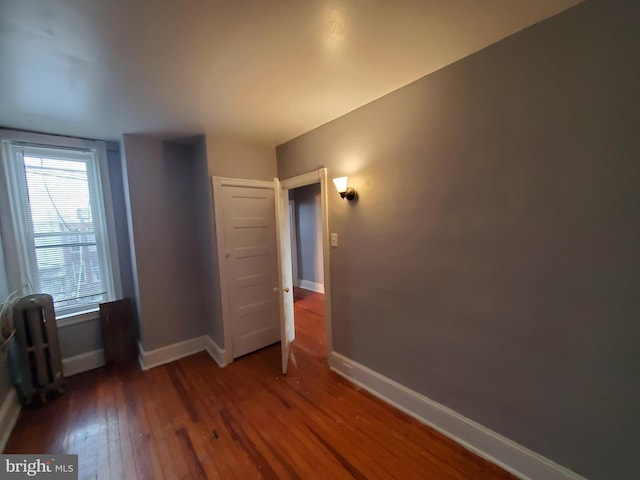 unfurnished bedroom featuring radiator heating unit and dark hardwood / wood-style floors