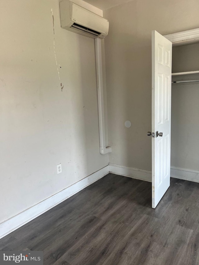 unfurnished bedroom featuring dark wood-type flooring, a wall mounted air conditioner, and a closet