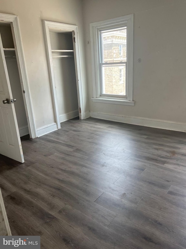 unfurnished bedroom with dark wood-type flooring and two closets