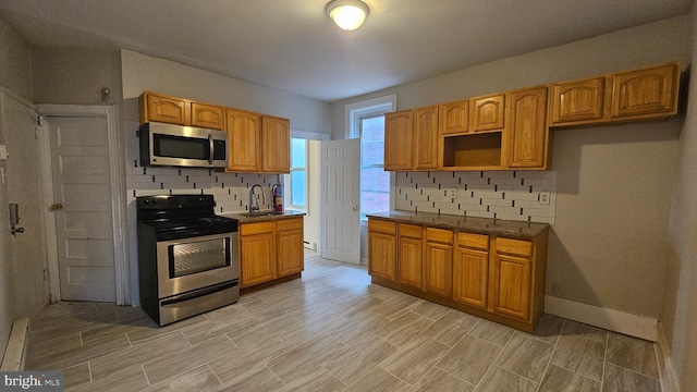 kitchen featuring sink, stainless steel appliances, tasteful backsplash, a baseboard radiator, and dark stone counters