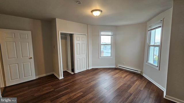 unfurnished bedroom with dark hardwood / wood-style flooring, multiple windows, a closet, and baseboard heating