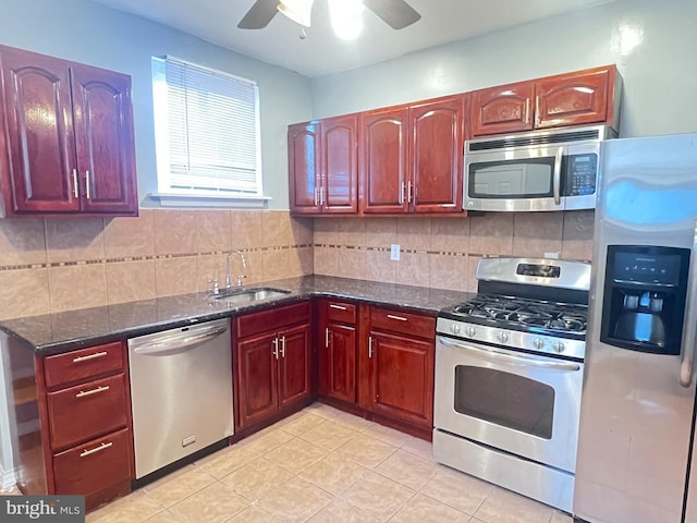 kitchen featuring appliances with stainless steel finishes, sink, decorative backsplash, dark stone counters, and ceiling fan