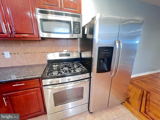 kitchen with dark stone countertops, light tile patterned floors, decorative backsplash, and appliances with stainless steel finishes