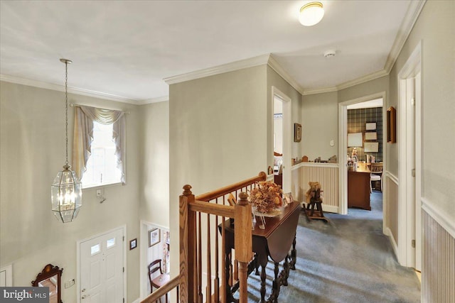 hall with dark colored carpet, ornamental molding, and an upstairs landing