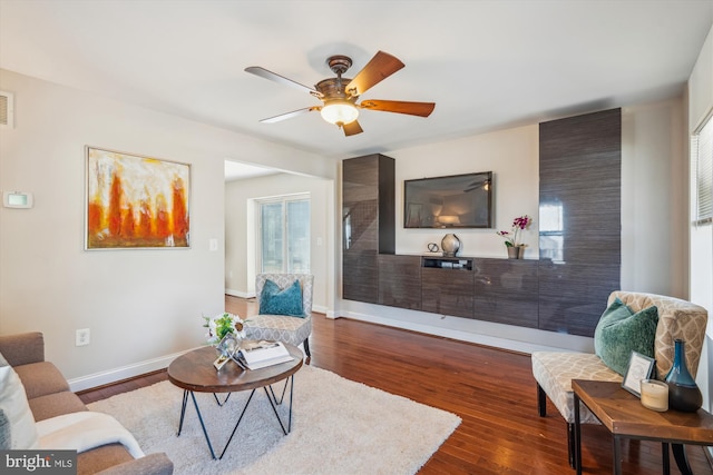 living area featuring visible vents, baseboards, a ceiling fan, and dark wood-style flooring