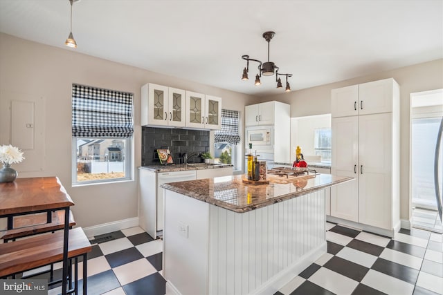 kitchen featuring white microwave, backsplash, glass insert cabinets, light floors, and white cabinetry