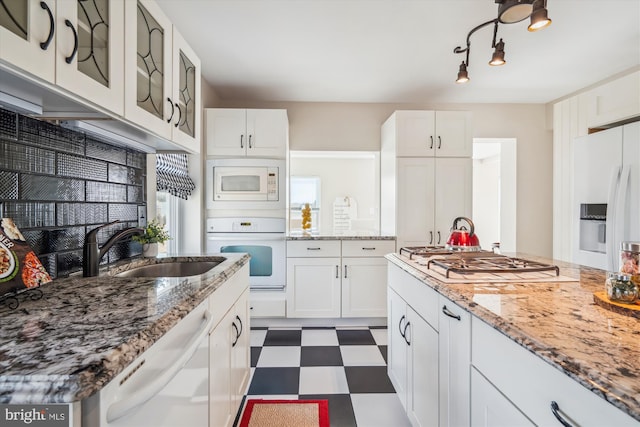 kitchen with a sink, white cabinetry, white appliances, dark floors, and glass insert cabinets