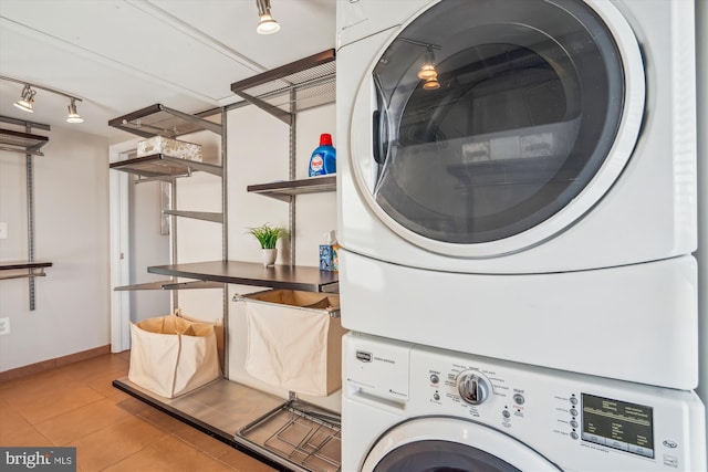 washroom featuring light tile patterned floors, baseboards, laundry area, track lighting, and stacked washer and dryer