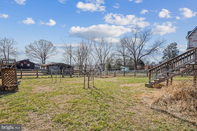 view of yard featuring a rural view, stairway, and fence