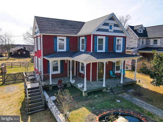 victorian-style house with a front yard, fence, covered porch, and roof with shingles