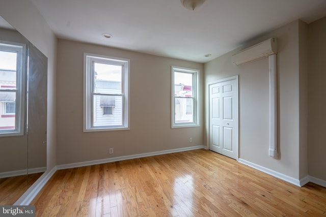 unfurnished bedroom with light hardwood / wood-style floors, a closet, and a wall mounted AC